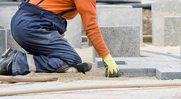 Construction worker on knees placing stone tiles in sand for pavement